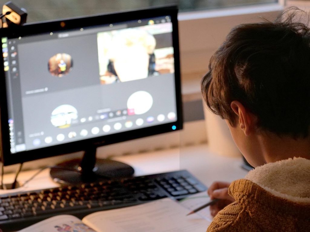 young boy taking notes while in online class