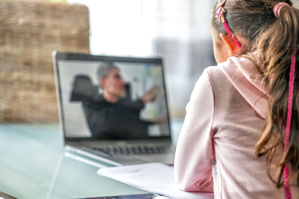 young girl listening and watching tutor on laptop