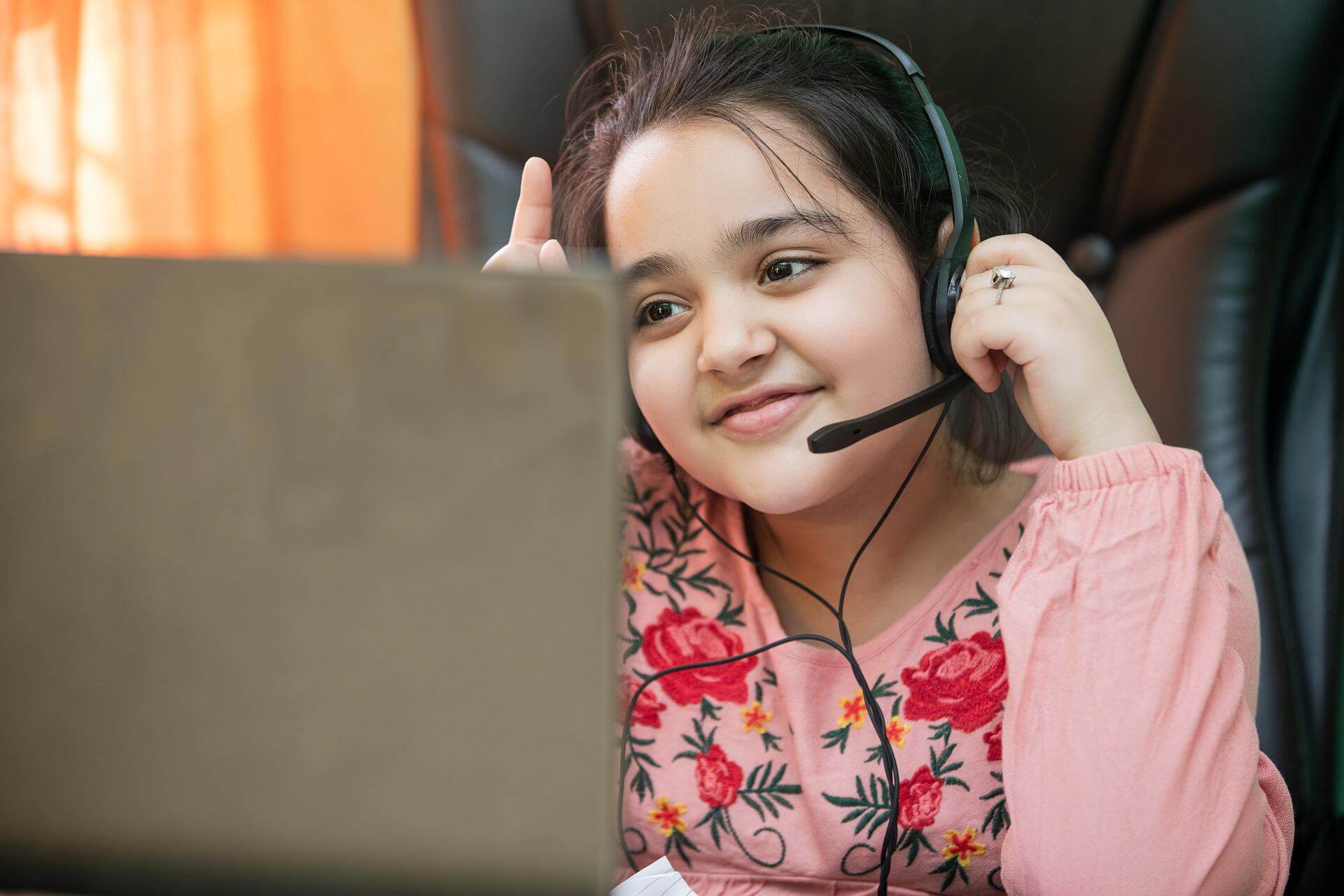 young girl wearing headset raising hand to ask question on laptop